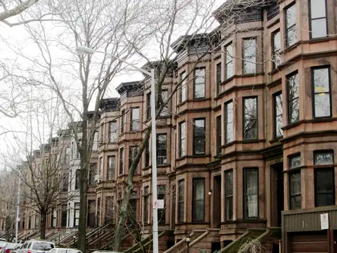 A row of brownstone townhouses with stoops and bay windows in Brooklyn