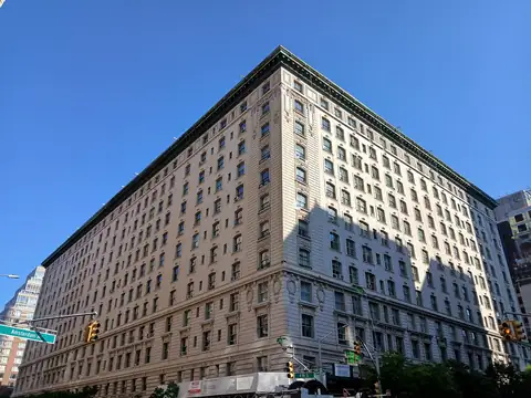 A tall pre-war apartment building of pale stone and brick on a sunny Manhattan corner