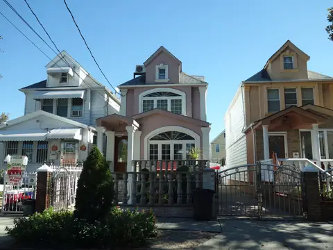 Three frame houses with peaked gables and front porches on a sunny street in Richmond Hill, Queens