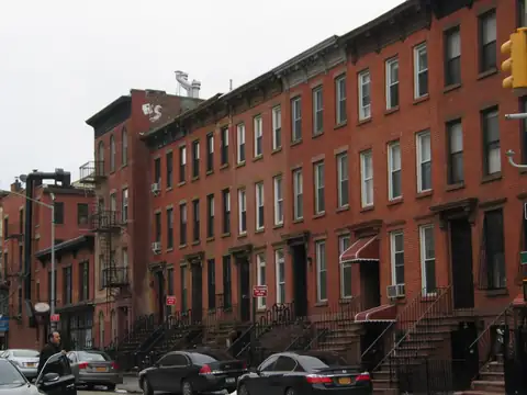 A row of red brick walk-up apartment buildings with stoops on a New York street