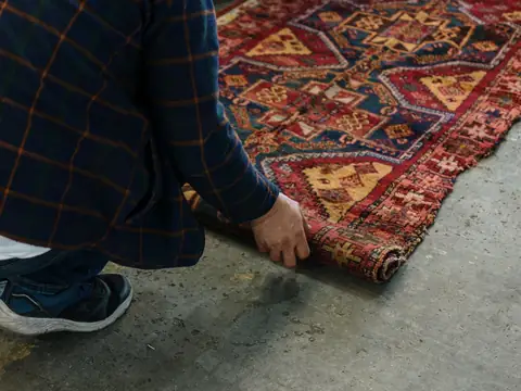 Hands unrolling a patterned rug across a bare concrete floor
