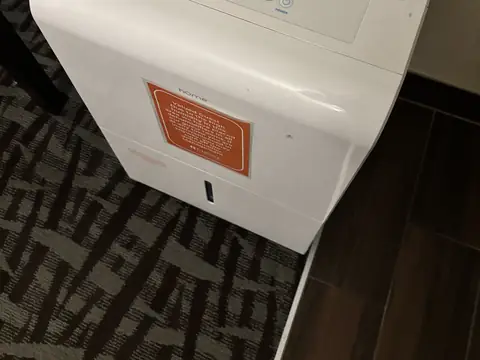 A white dehumidifier running on the carpet of a bedroom