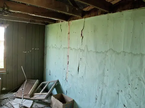 A water line and stains across a wall under a ceiling opened to the joists