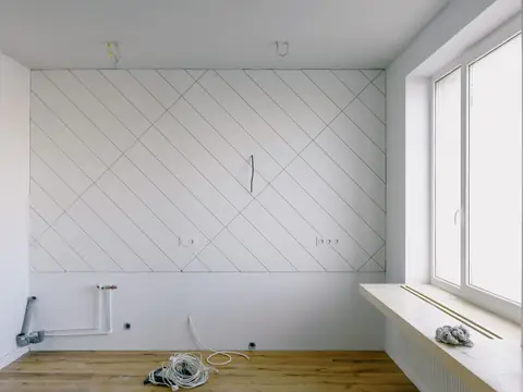 A newly built wall in a room under repair, a pipe and cables coming out at floor level