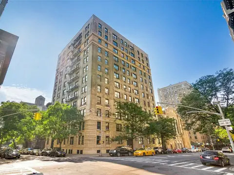 A tall pre-war apartment building of tan brick rising over a tree-lined Manhattan corner