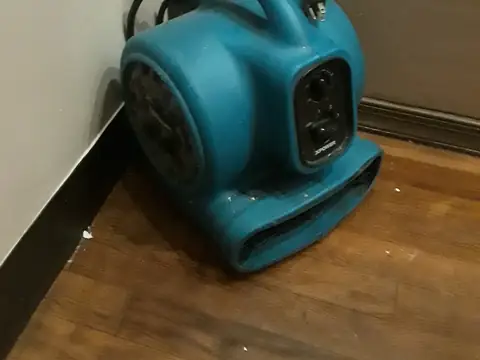 A blue air mover set in the corner of a room, blowing along the base of the wall