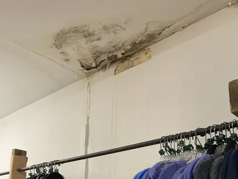 A water-stained, spotted ceiling corner above a clothes rail in a closet
