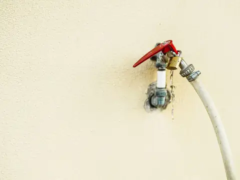 A valve with a red handle on a wall, a hose attached and water dripping from the joint