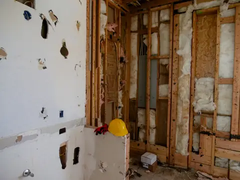 A wall with the drywall stripped away to the wooden studs and insulation
