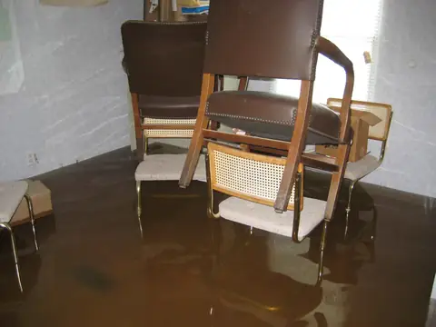 Chairs stacked on a table above brown water standing across the floor of a room