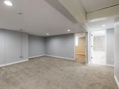 An empty finished lower level with carpet, white walls and recessed lights
