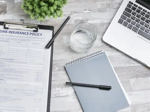 A home insurance policy, a notebook and a laptop laid out on a desk