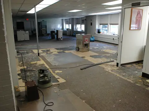 Dehumidifiers and drying equipment set out across a large room with the floor covering pulled up