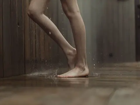 Water spreading across a dark wooden floor around a bare foot